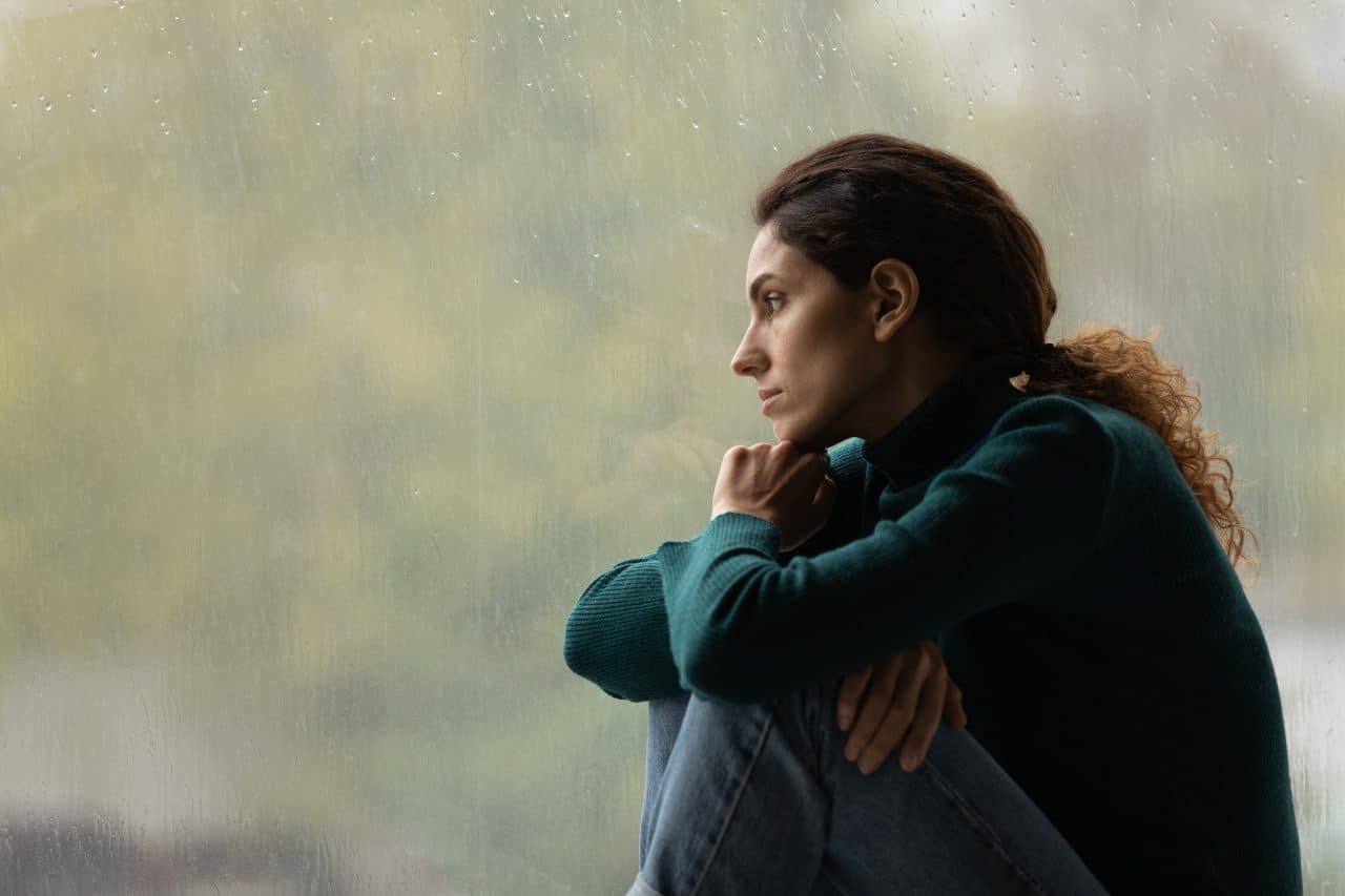 Side view of a morose woman looking out rainy window