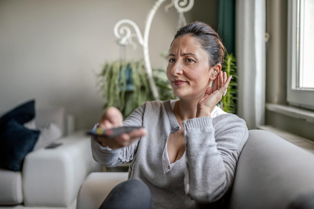 Young woman adjusting her hearing aid while watching TV.